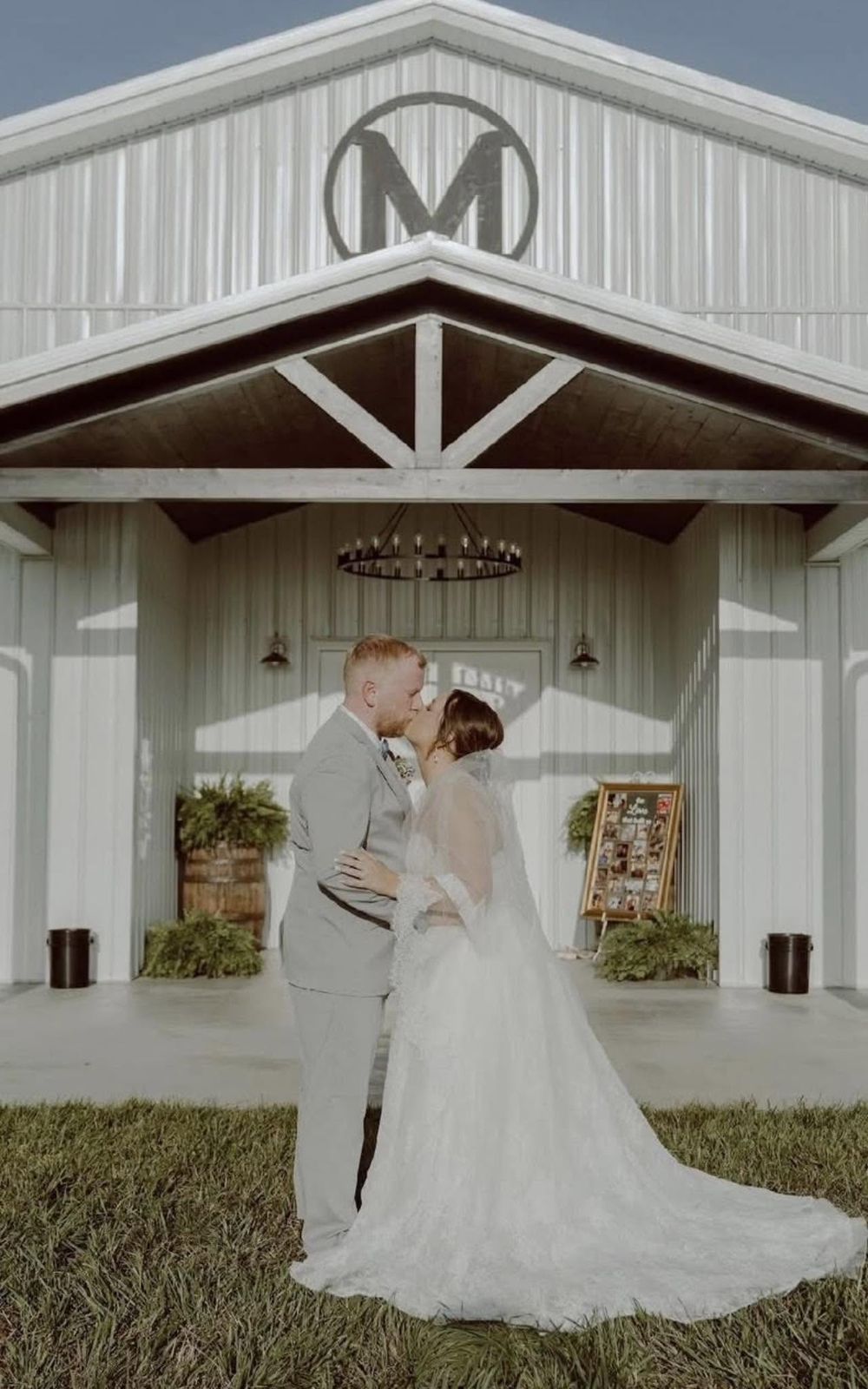 Bride and groom kissing beneath the entrance chandelier of the Mirewood barn