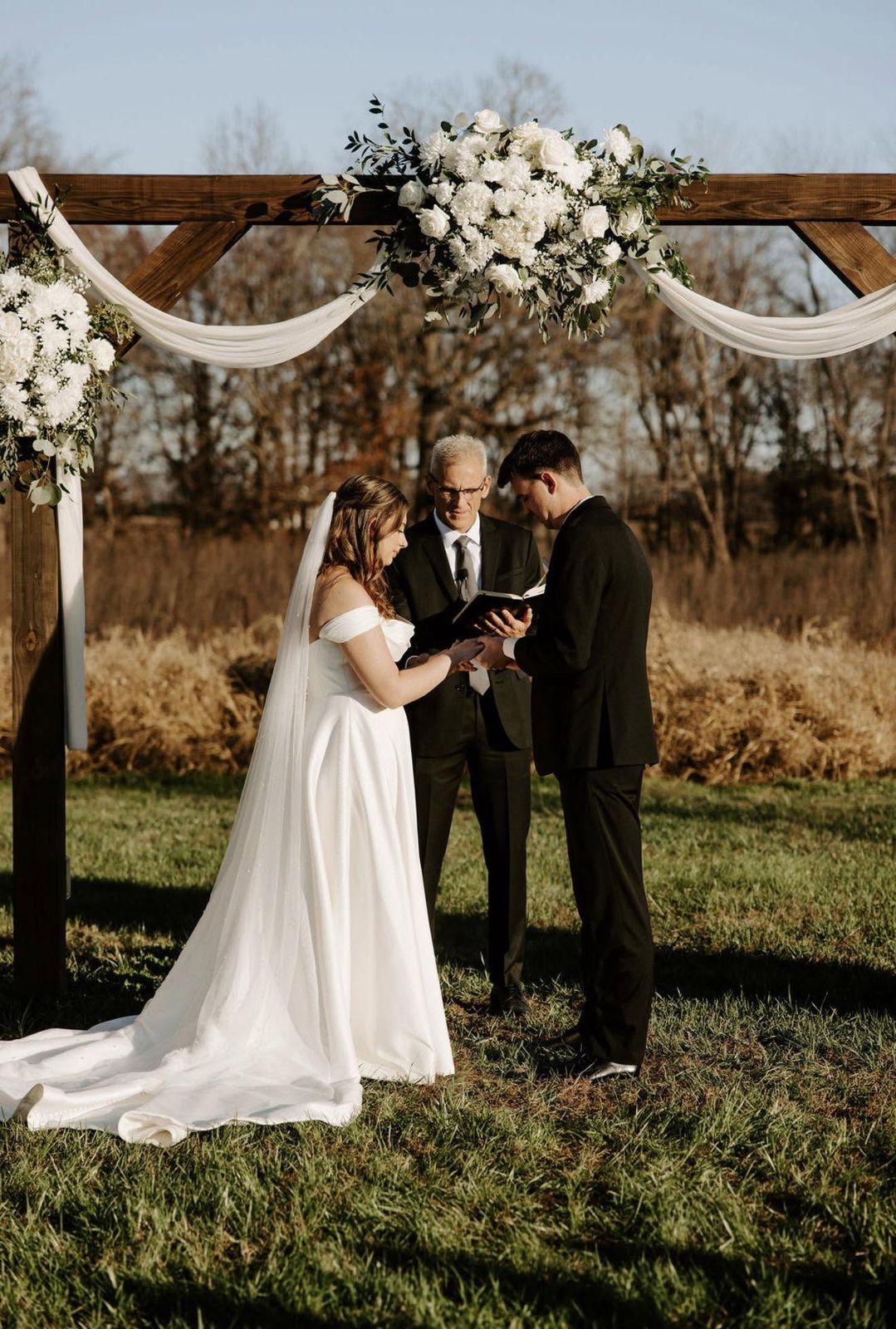 Bride and groom exchanging vows under a floral arch at their outdoor ceremony