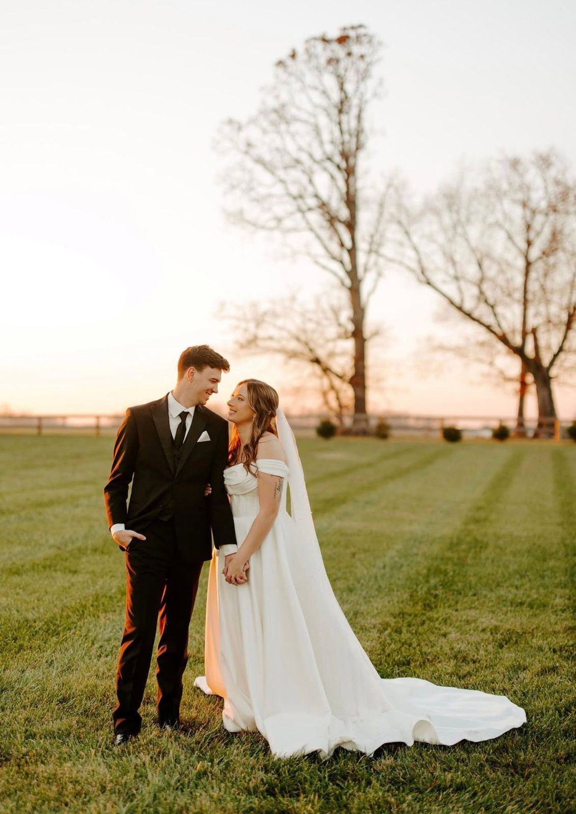 Bride and groom smiling at each other in the open field at sunset