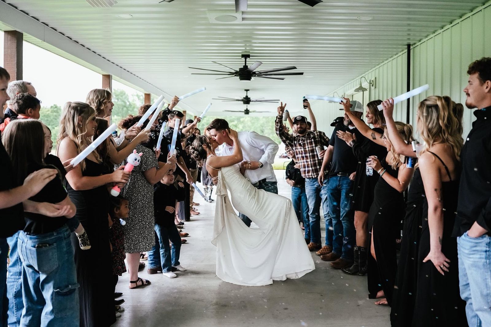 Guests lining the covered walkway cheering the newlyweds with glow sticks and bubbles