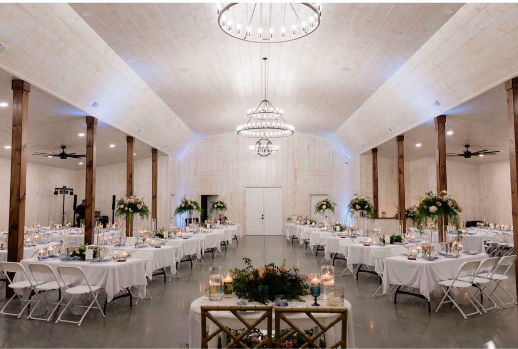 White wood barn reception hall interior with wagon-wheel chandeliers and elegant table settings