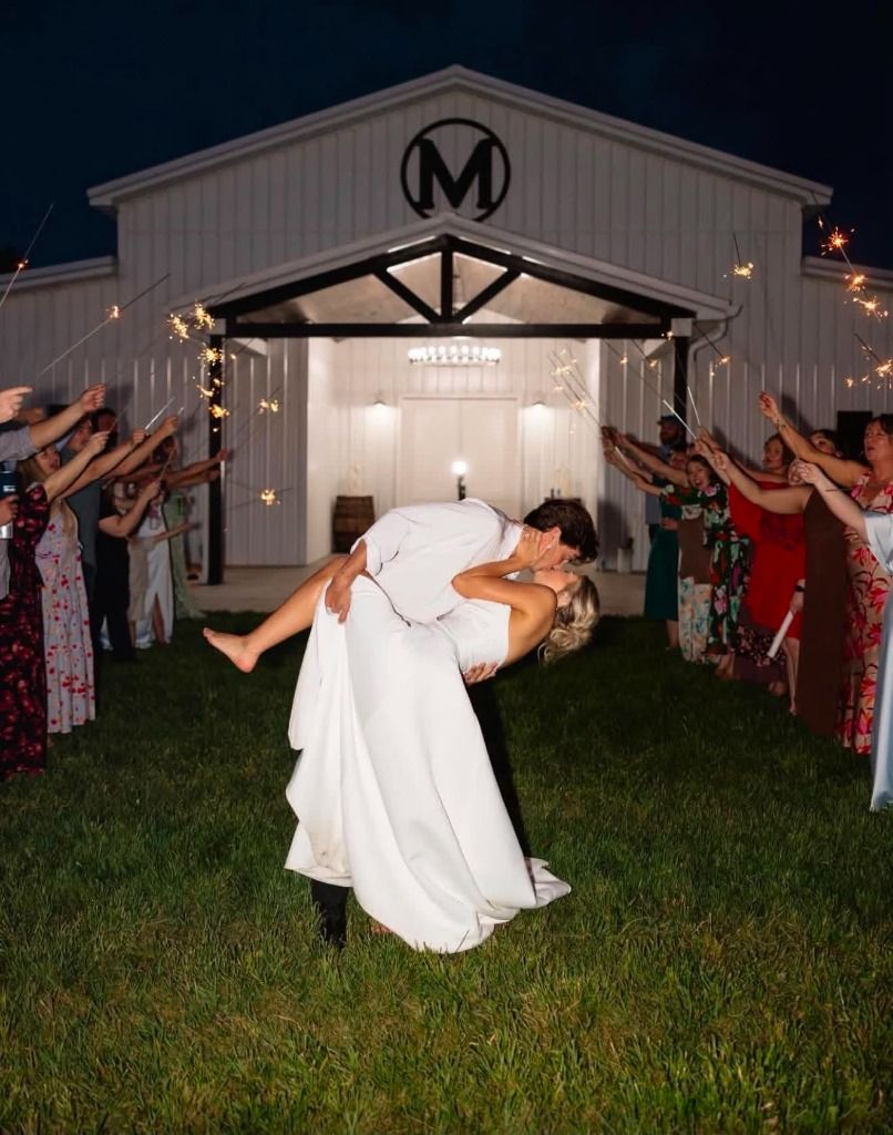 Bride and groom dipping and kissing outside the white barn venue during a sparkler send-off